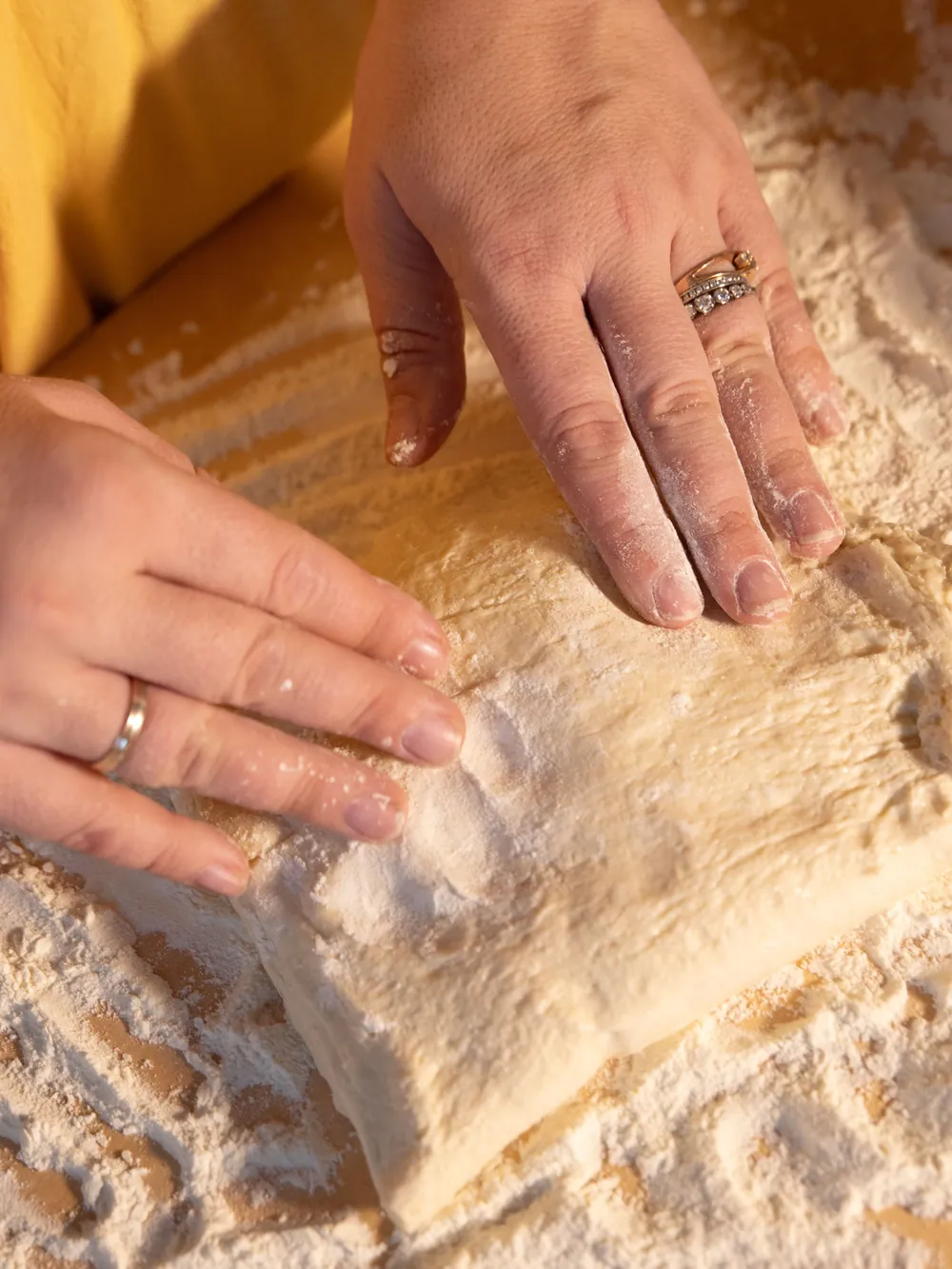 Two floury hands pressing a round of pizza dough on a wooden board