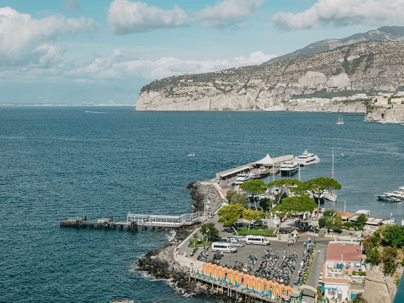 A marina and jetty on the Sorrento shore seen from above, with pale limestone cliffs rising across the blue water